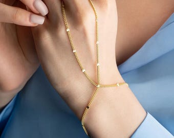 May include: A gold chain bracelet with small square accents. The bracelet is designed to wrap around the wrist and then extend up the arm, ending with a ring that can be worn on the finger.