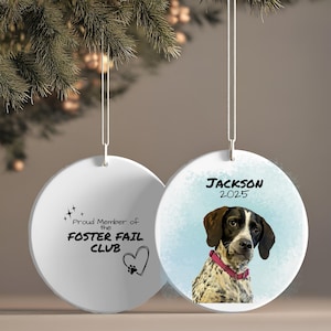 Peut inclure: Ornement de Noël en céramique blanche avec un portrait de chien et le nom "Jackson 2025". Le chien a des marques marron et noires et porte un collier rose. L'autre côté dit "Proud Member of the FOSTER FAIL CLUB" avec un cœur d'empreinte de patte.