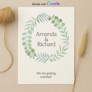 Puede incluir: Una invitación de boda con los nombres "Amanda & Richard" dentro de una corona de eucalipto en acuarela. El texto "We are getting married!" está debajo. Un carrete de hilo y una flor seca están a ambos lados.