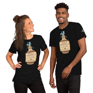 May include: Two black t-shirts with a graphic of a potion bottle labeled "Potion of Caffeine +3". The bottle is brown with a blue liquid and steam coming out of the top. The text on the label is in a vintage style font.