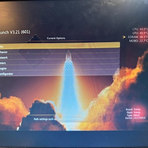 K&ouml;nnte beinhalten: Ein Computermonitor zeigt die DashLaunch V3.21 Softwareoberfl&auml;che mit einem Raketenstart-Hintergrund. Das Men&uuml; listet Paths, Behavior, Network, Timers, Plugins und Configurator auf. Die Systemtemperaturen f&uuml;r CPU, GPU, EDRAM und MOBO sind sichtbar.