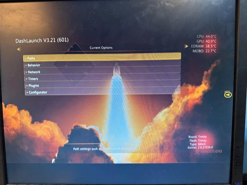 K&ouml;nnte beinhalten: Ein Computermonitor zeigt die DashLaunch V3.21 Softwareoberfl&auml;che mit einem Raketenstart-Hintergrund. Das Men&uuml; listet Paths, Behavior, Network, Timers, Plugins und Configurator auf. Die Systemtemperaturen f&uuml;r CPU, GPU, EDRAM und MOBO sind sichtbar.