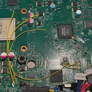 K&ouml;nnte beinhalten: Ein gr&uuml;nes Xbox 360-Mainboard mit verschiedenen elektronischen Komponenten, darunter ein Hauptprozessor mit Microsoft-Branding, silberne Kondensatoren und mehrere d&uuml;nne gelbe Dr&auml;hte, die auf die Oberfl&auml;che der Platine gel&ouml;tet sind.