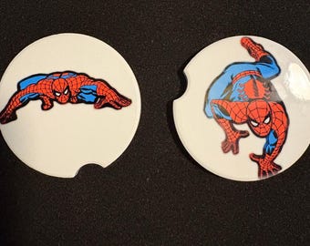 May include: Two white car coasters featuring Spider-Man in action poses. One coaster shows Spider-Man crawling, and the other shows him in a crouching position. The superhero is depicted in his classic red and blue suit.