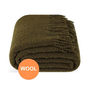 Op de afbeelding: Gevouwen olijfgroene wollen deken met een getextureerd oppervlak en een gefranjerde rand. De deken is strak opgevouwen, wat de zachte textuur laat zien. Een oranje cirkel met het woord "WOOL" is zichtbaar.