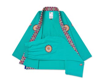 May include: A teal kimono-style jacket featuring a vibrant geometric pattern along the collar and cuffs. The garment includes a circular mandala-style embroidery on the sleeve and back, with the text ML printed on the interior neck label.