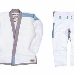May include: A white Brazilian Jiu-Jitsu gi set consisting of a jacket and pants. The jacket features a grey collar, light blue shoulder accents, and the text Albino & Preto with an AP logo. The pants are white with grey and light blue detailing.