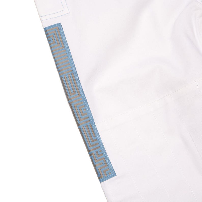 May include: A white garment featuring a vertical side panel with a light blue and tan geometric maze-like pattern. The fabric appears smooth and opaque, with visible stitching along the seam where the patterned panel meets the plain white section.