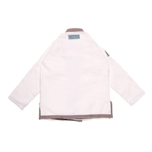 May include: A white martial arts gi jacket featuring long sleeves, a sturdy collar, and grey trim along the bottom hem. A small rectangular blue patch is positioned at the center of the neckline, and a grey triangular logo patch is on the left sleeve.