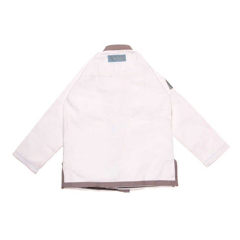 May include: A white martial arts gi jacket featuring long sleeves, a sturdy collar, and grey trim along the bottom hem. A small rectangular blue patch is positioned at the center of the neckline, and a grey triangular logo patch is on the left sleeve.