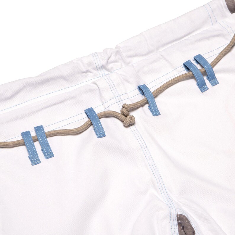 May include: White pants featuring a light blue drawstring waistband with light blue belt loops and a tan cord threaded through them. The pants have visible light blue stitching along the seams and a tan fabric detail at the bottom hem area.