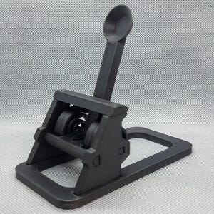 May include: A black miniature trebuchet model, featuring a launching arm with a small cup, a base, and a complex system of wheels and levers. The model is made of a matte black material.