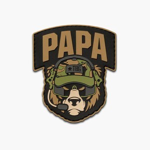 May include: A patch with a bear design wearing a camouflage helmet and sunglasses, with the word "PAPA" in tan letters above. The bear has a headset with a microphone. The patch is black with tan and green details.