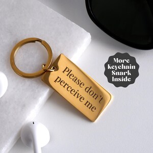 May include: Gold keychain with a rectangular tag that reads "Please don't perceive me".