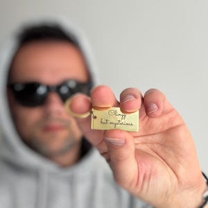 May include: A gold-colored metal keychain with the text "Clingy but mysterious" engraved on it.
