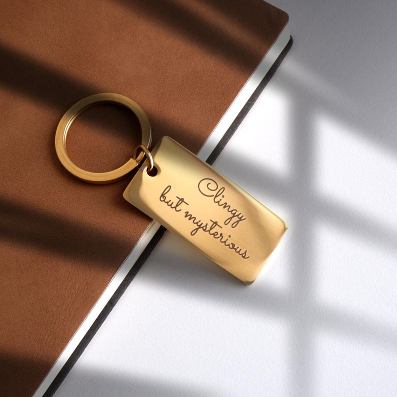 May include: Gold-colored keychain with a rectangular tag that reads "Clingy but mysterious".