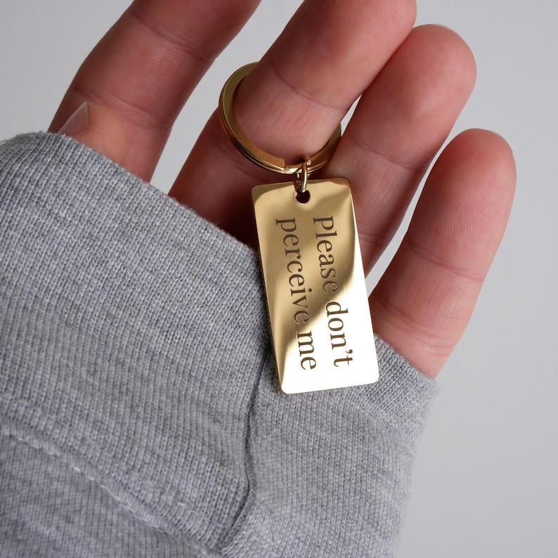 May include: Gold-colored keychain with a rectangular tag that reads "Please don't perceive me".