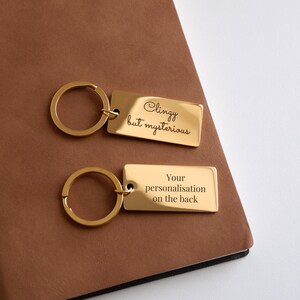May include: Gold-toned keychain with a rectangular tag that reads "Clingy but mysterious". The back of the tag has space for personalization.