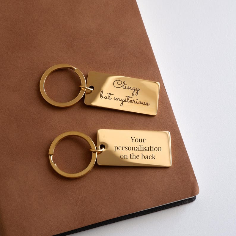 May include: Gold-toned keychain with a rectangular tag that reads "Clingy but mysterious". The back of the tag has space for personalization.
