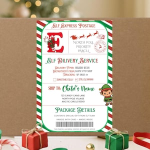 May include: A brown cardboard box with a festive Christmas label. The label features text including "Elf Express Postage" and "Elf Delivery Service." A cartoon elf is on the label. The box is decorated with red and green ribbons and small gift boxes.