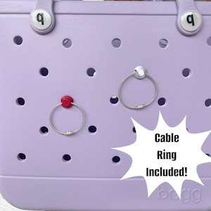 May include: A lavender tote bag with two cable rings attached. One ring has a red connector and the other has a silver connector. The text "Cable Ring Included!" is written on a white starburst.