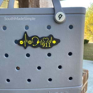 May include: Gray and yellow  "911" heart beat design on a gray  Bogg bag.