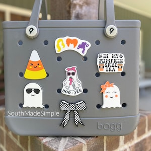 May include: A gray tote bag with a variety of Halloween-themed stickers, including a ghost, a candy corn, a bow, and a coffee cup with the text "In My Pumpkin Spice Era".