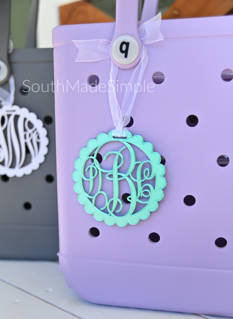 Peut inclure: Un sac fourre-tout lavande avec un ruban blanc et un charme monogramme vert clair. Le charme a un bord festonn&eacute; et le monogramme est les lettres "B.E." Le sac fourre-tout a le num&eacute;ro "9" sur le devant.