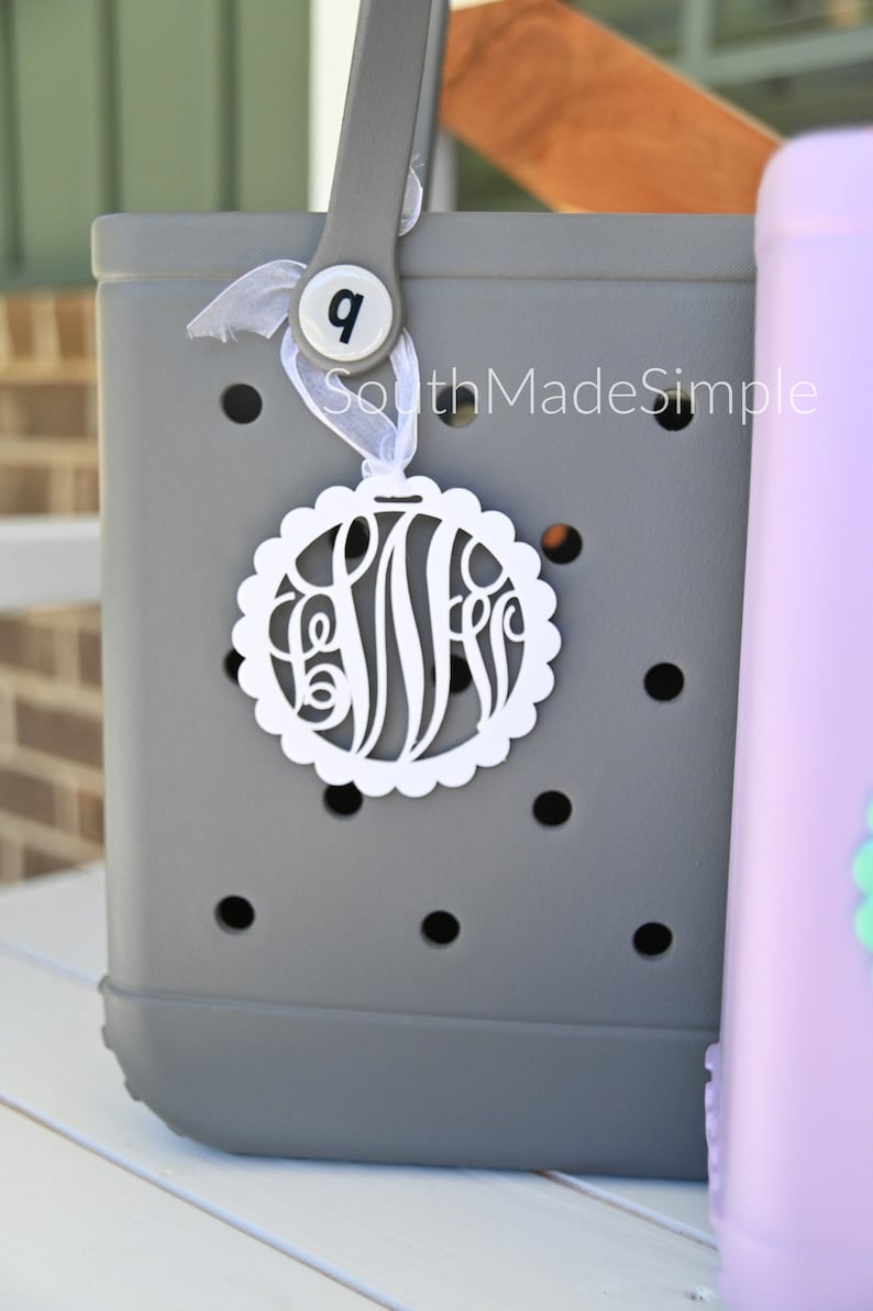 Peut inclure: Un sac cabas gris avec un charme monogramme blanc et un ruban blanc. Le sac a une poign&eacute;e grise et le num&eacute;ro "9" sur un cercle blanc attach&eacute; &agrave; la poign&eacute;e. Le texte "SouthMadeSimple" est imprim&eacute; sur le sac.