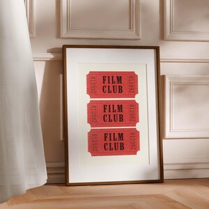 May include: A framed print with three red tickets that say "Film Club" in black text. The tickets are arranged vertically in a row.