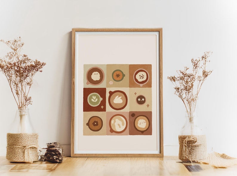 May include: Framed art print with a grid of nine coffee cup designs. Each square displays a different latte art design in brown, beige, and green. The print is on a wooden surface, with dried flowers in glass vases on either side.