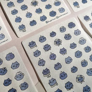 May include: Sheets of stickers featuring blue cat illustrations with various accessories. The stickers have a watercolor effect and are arranged on a white background. The text "PurpleTimes.art" is visible on some stickers.