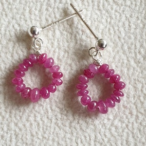 May include: A pair of silver earrings with pink ruby gemstone beads in a circle shape.