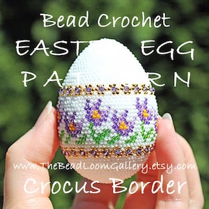 以下が含まれることがあります： 紫と金のクロッカス模様の縁取りが施された白いビーズ製のイースターエッグ。卵は手で持たれており、卵の下には「Bead Crochet Easter Egg Pattern Crocus Border」というテキストが表示されています。