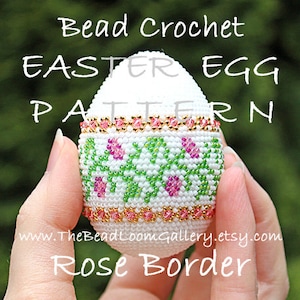 以下が含まれることがあります： 緑とピンクの花柄と、ゴールドとピンクのバラの縁取りが施された白いビーズのイースターエッグ。ビーズクロシェイースターエッグパターン。www.TheBeadLoomGallery.etsy.com ローズボーダー