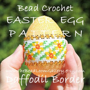 以下が含まれることがあります： 「Bead Crochet Easter Egg Pattern Daffodil Border」の文字が入ったビーズのイースターエッグパターン。卵は黄色で、白、緑、黄色、オレンジの花柄のデザインです。金のビーズが花の帯の上部と下部を縁取っています。