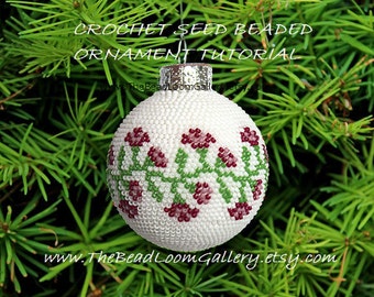 Op de afbeelding: Witte, met kralen bezette kerstbal met een groen en bordeauxrood bloemenmotief. De bal hangt aan een groene dennentak. De tekst "CROCHET SEED BEADED ORNAMENT TUTORIAL" staat bovenaan de afbeelding. De tekst "www.TheBeadLoomGallery.etsy.com" staat onderaan de afbeelding.