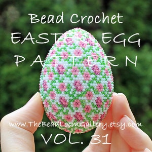 Puede incluir: Un patrón de huevo de Pascua con cuentas en rosa, verde y blanco, sostenido en una mano. El huevo está cubierto con un diseño floral. El texto en la imagen dice "Bead Crochet Easter Egg Pattern" y "VOL. 31". La dirección del sitio web también es visible.