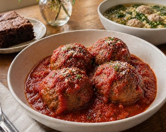Puede incluir: Primer plano de un cuenco lleno de cuatro grandes albóndigas cubiertas con una rica salsa de tomate roja. Las albóndigas están espolvoreadas con una guarnición. También se ve un cuenco de sopa y un brownie.