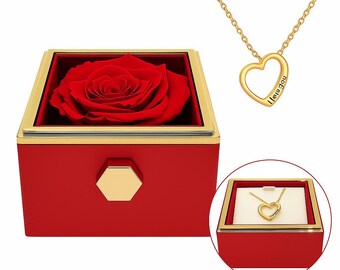 Può includere: Una rosa rossa conservata in una scatola rossa con bordo dorato e un coperchio esagonale dorato. La scatola è dotata di una collana d'oro con un ciondolo a forma di cuore su cui è inciso "Ti amo".