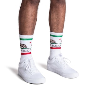 May include: White socks with a red, white and green California flag design featuring a bear and the text "PUBLIC CA". The socks are worn with white trainers.