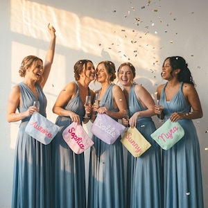 May include: Six women in blue dresses laugh and hold personalized cosmetic bags. Each bag is a different pastel color and embroidered with a name: Aurora, Sophia, Isolde, Sunny, and Nyra. Confetti falls from above.