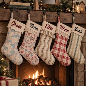 Puede incluir: Cinco calcetines navideños de tela colgados en fila, cada uno con un puño color crema bordado con los nombres: Grace, Nora, Ellie, Mom y Dad. Los calcetines muestran patrones variados que incluyen hojas de roble azules, flores rosas, rayas onduladas, cuadros rojos y rayas verdes.