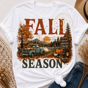 Op de afbeelding: Een wit t-shirt met een grafische print met de tekst FALL SEASON. Het ontwerp bevat een vintage blauwgroene vrachtwagen vol pompoenen, een zonsondergang, bergen, bomen en een houten wegwijzer met de woorden COZY DAYS, CRISP AIR, PUMPKIN SPICE en AUTUMN VIBES.