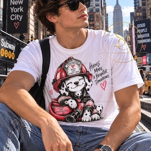 Könnte beinhalten: Ein weißes T-Shirt mit einer Grafik eines Dalmatiner-Welpen, der einen roten Feuerwehrhelm und eine Jacke trägt und auf einem roten Feuerwehrschlauch liegt. Der Text lautet FIREFIGHTER BRAVE KIND ALWAYS THERE, HEROES MAKE A BRIGHTER TOMORROWS und SUPPORT OUR FIREFIGHTERS.