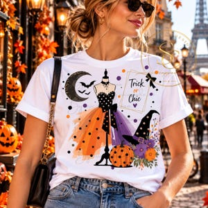 Op de afbeelding: Een wit t-shirt met een grafische print van een paspop die een lijfje met stippen en een gelaagde oranje en paarse rok draagt. Het ontwerp bevat een maansikkel, vleermuizen, een pompoen, een heksenhoed, bloemen en de tekst Trick or Chic.