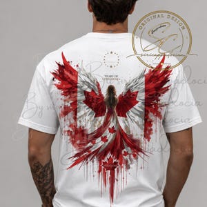 Op de afbeelding: Een wit t-shirt met een rugprint van een figuur met grote vleugels in de kleuren van de Canadese vlag. Het ontwerp bevat rode esdoornbladeren, een cirkel van sterren en de tekst YEARS OF FREEDOM en FREEDOM in een aquarel-stijl.