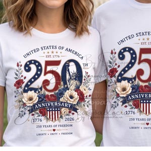 Op de afbeelding: Witte T-shirts met een patriottisch ontwerp ter viering van de 250e verjaardag van de Verenigde Staten. Het ontwerp bevat de tekst "United States of America", de jaren 1776 en 2026 en bloemelementen in rood, wit en blauw.