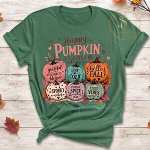 Op de afbeelding: Een saliegroen t-shirt met een afbeelding van vijf pompoenen in roze, oranje en blauwgroene tinten. De tekst luidt Happy PUMPKIN Season, grateful thankful blessed, STAY COZY, hello FALL, SPOOKY vibes, PUMPKIN SPICE & everything nice en GOOD VIBES ONLY.