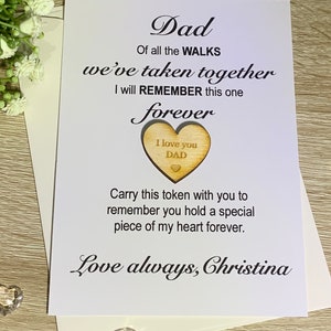 May include: A white card with black text that reads "Dad, Of all the WALKS we've taken together I will REMEMBER this one forever." A wooden heart with the text "I love you DAD" is attached to the card. The card is signed "Love always, Christina."